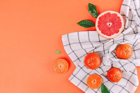 Fresh ripe mandarins and grapefruit with green leaves on white towel on orange background with space...