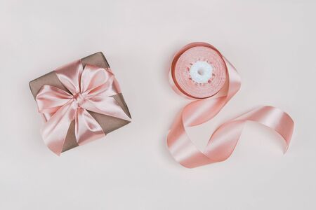Gift box wrapped in craft paper with perfect pink ribbon on pale pink rustic background. Festive concept, top view.の写真素材