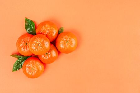 Pile of fresh ripe mandarins with green leaves on orange background. Copy space, top view.の写真素材