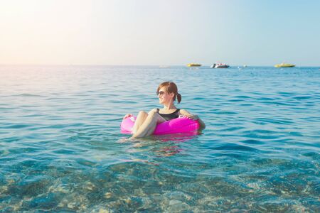 Young woman with pink swimming ring at the sea in sunny day. Summer vacation concept. Back view.