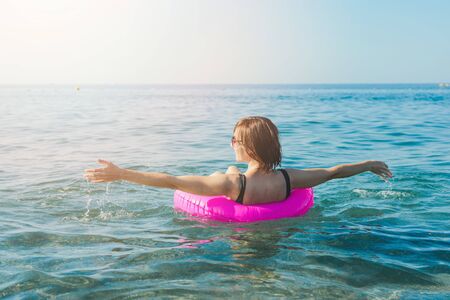 Young woman with pink swimming ring at the sea in sunny day. Summer vacation concept. Back view.の写真素材
