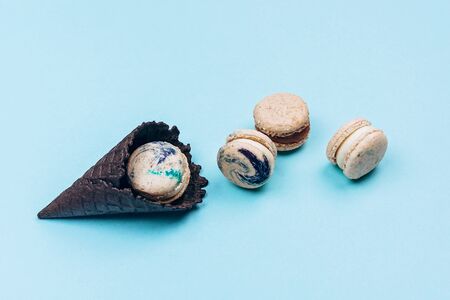 Assorted macaroons in black ice-cream horn on pastel blue background with copy space. Creative and moody picture. Top view, flat lay.の写真素材