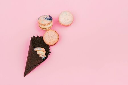 Assorted macaroons in black ice-cream horn on pastel pink background with copy space. Creative and moody picture.の写真素材