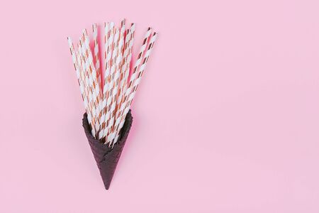 Cocktail straws with golden stripes in black ice-cream horn on pastel pink background with copy space.の写真素材