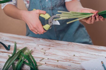 Hands of young woman florist cutting fresh flowers making bouquet of fleur-de-lises on table. Close...