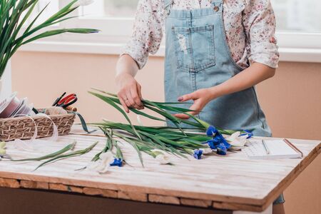 Hands of young woman florist working with fresh flowers making bouquet of fleur-de-lises on table. Close up.の写真素材