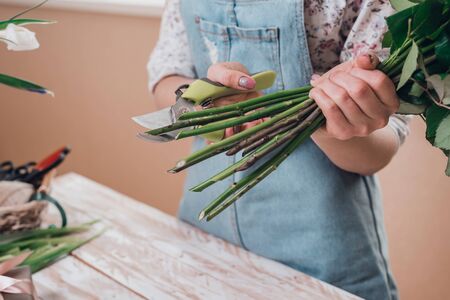 Hands of young woman florist cutting fresh flowers making bouquet of roses on table. Close up.の写真素材