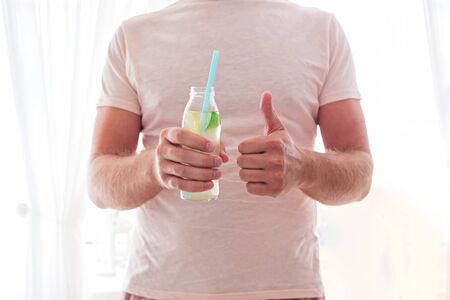 Man drinks lemonade through a straw from glass bottle. Cropped.