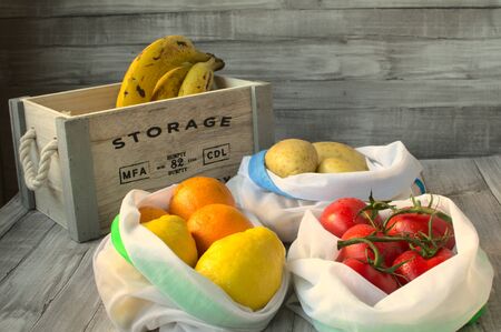 There are three white cloth bag, one with tomatoes, other with oranges and lemons and another with...