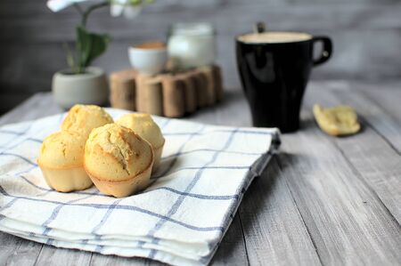 Close up of some homemade lemon muffins, at the bottom a cup of coffee with milk, a piece of muffin, a white orchid and one bowl with sugar and other with cinnamonの写真素材