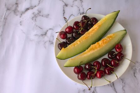 Two slices of melon and cherries on a white plate.の写真素材