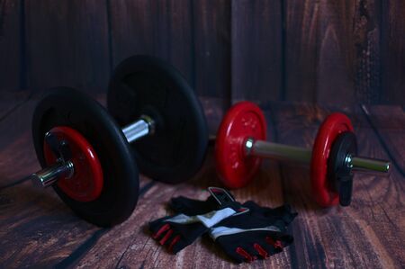 Red and black dumbbells next to black and red weight glovesの写真素材