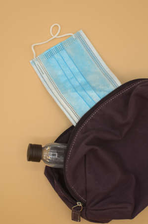 Top view, purple makeup bag, sticking out a small bottle of hand gel and surgical mask.