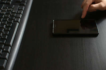Woman using smart phone in front of keyboard. Woman hand
