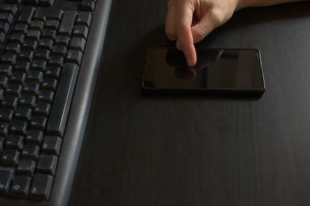 Woman using smart phone in front of keyboard