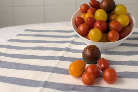 Close up of white bowl with selection of assorted cherry tomatoes, more tomatoes on white and blue plaid cloth.の写真素材