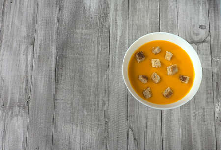 Close up of pumpkin and carrot cream with croutons on wooden table.の写真素材