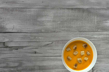 Close up of pumpkin and carrot cream with croutons on wooden tableの写真素材
