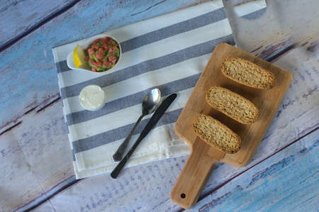 Three toasted buns on wooden table, next to a small bowl with cream cheese and another with...