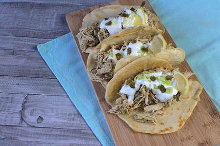 Close up of homemade wheat tortillas stuffed with chicken in avocado sauce, top garnished with...