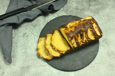 Close up of apple sponge cake with pine nuts on a gray stone tray, on a stone base