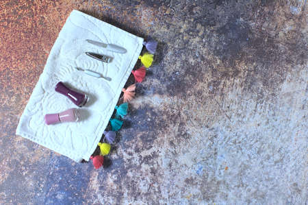 Manicure set consisting of cuticle pusher, nail clipper, nail file and nail polish on a white towel with colored tassels, on a rusty-looking backgroundの写真素材