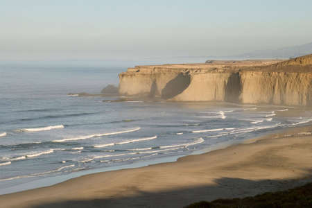 Shadows retreat across beach as sun rises over Tunitas Creek Beach in rural San Mateo county, California.の写真素材