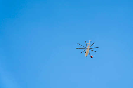 Firefighters Helicopter in Flight with Water Basket against Blue Skyの写真素材