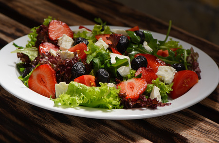 Salad, strawberries and cheese on a white plateの写真素材