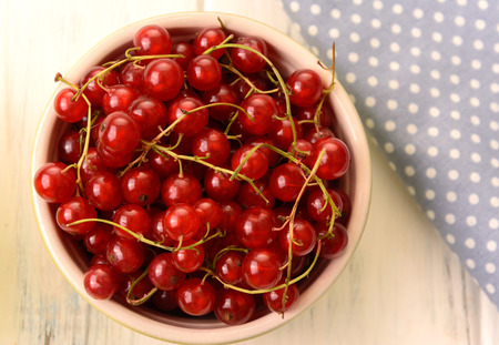 Red currants in a plate near the napkin on white wooden background