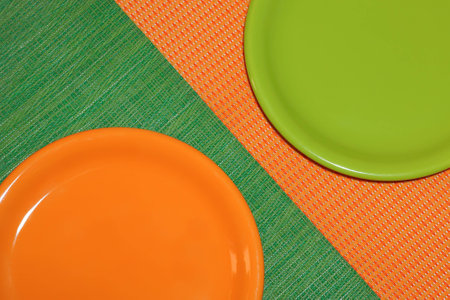 Two empty plates. Orange stands on a green napkin,green on orange napkin.arranged diagonally. top viewの写真素材
