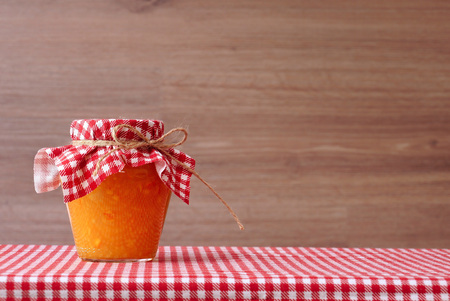 Orange jam in a glass jar on a red checkered tablecloth. Wooden backgroundの写真素材