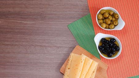 Black and green olives in oil and slices of cheese on a wooden background. View from above. Free space for textの写真素材