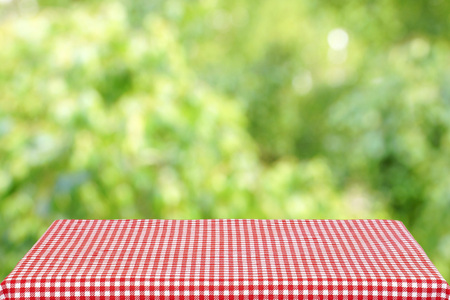 Empty table with a red checkered cloth in the summer garden. Blurred background.