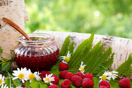 Raspberries. An open jar with jam and raspberries among forest grasses.