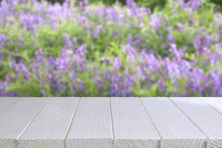 Empty table on the background of a flowering garden. White wooden table for placing your products. Blurred violet background.の写真素材