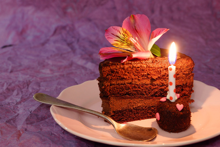 Chocolate cake. A piece of cake with a candle and a lily flower. Lilac background.の写真素材