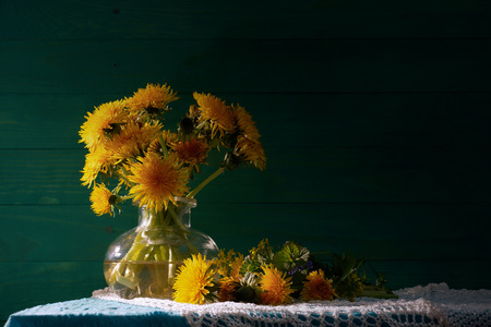 Dandelions in a glass vase. Bouquet of wilting dandelions. Green wooden background. Rustic still lifeの写真素材
