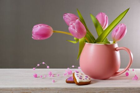 Bouquet of tulips on a gray background. Tulips in a pink cup and two gingerbread cookies on a white tableの写真素材