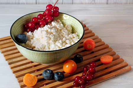 Light breakfast with cottage cheese. Homemade grained cottage cheese with berries on a white wooden tableの写真素材