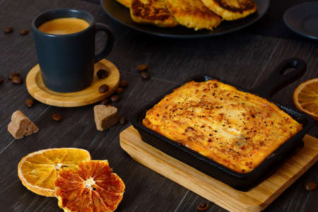 Curd casserole and a cup of coffee on a black table. Breakfast serving.