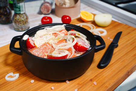 Salmon cooking. Pieces of raw fish with onions and tomatoes marinated in cream