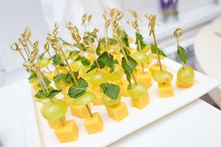 Buffet snacks, canapes placed on plate. Snacks with meat, fruits, cheeses and prawns. To greet...