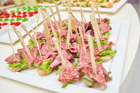 Buffet snacks, canapes placed on plate. Snacks with meat, fruits, cheeses and prawns. To greet...