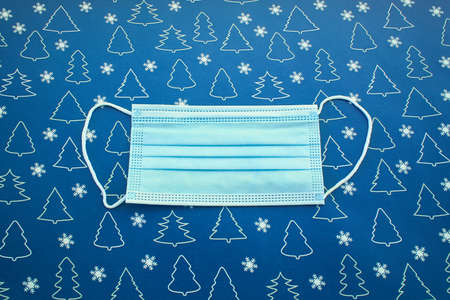 Face mask on the blue New Year background with Christmas trees. Coronavirus Christmas background. Black and white photography, close upの写真素材