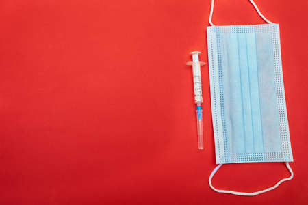 Face mask and medical syringe on the red background. Coronavirus.  close up