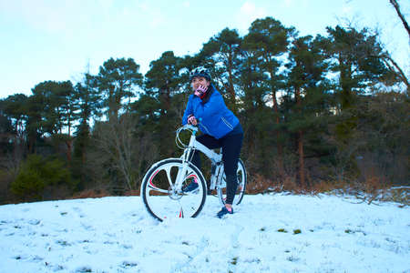 Extreme cyclist rides in the winter snowy forest. joyful riders in bright, modern outfit on light carbon mountain bike ride in the fresh pure snow in the woods snowy and wild in the city parkの写真素材