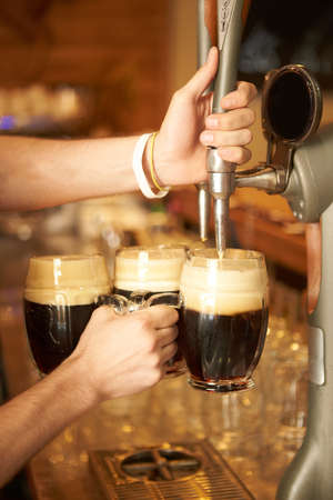 The bartender pours a beer in a beer cups. Draught beer.