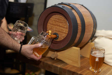 The bartender pours a beer in a beer cups from barrel. Draught beer.