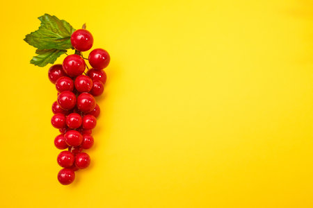 Decorative red bunch of grapes with green leaves isolated on yellow background.